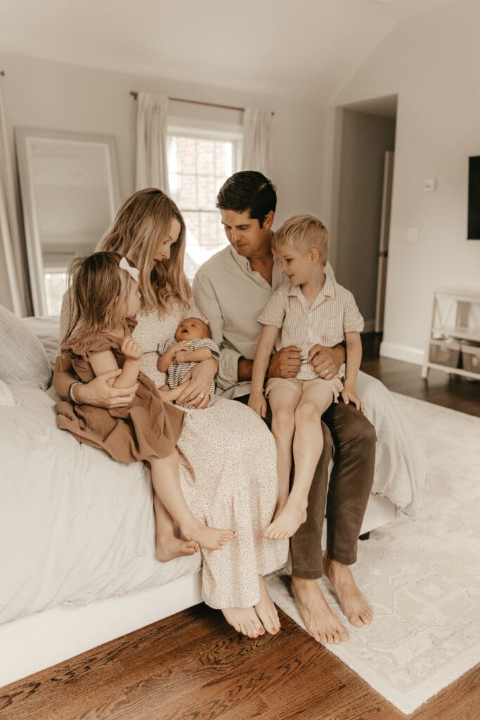 Parents sitting on a bed with three young children, including a newborn and siblings snuggled close — cozy and connected in-home family session in Summit, NJ.