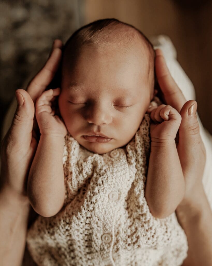 Newborn baby peacefully sleeping with hands gently cradling their head, wearing a textured cream knit romper — detailed lifestyle newborn portrait in Morris County, NJ.
